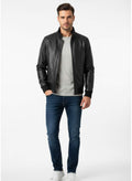 Man wearing a black leather jacket, gray shirt, and blue jeans on a white background