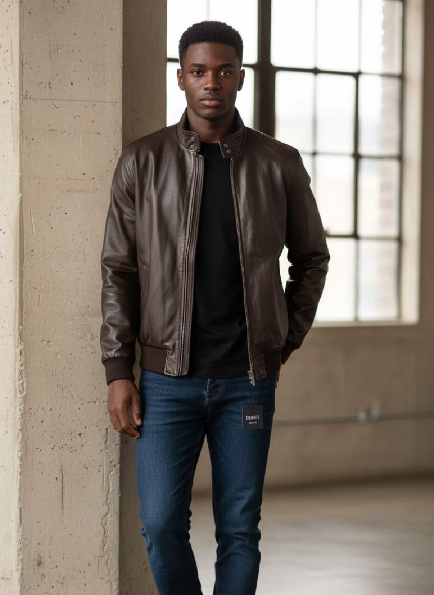Man wearing brown leather bomber jacket, black tee, blue jeans, white sneakers in industrial loft