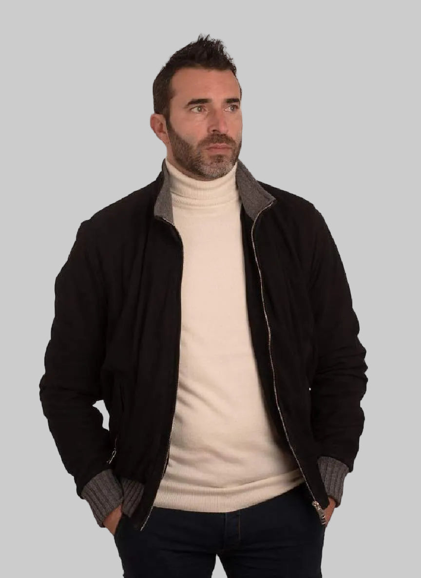 Man wearing a black jacket over a beige turtleneck on a white background