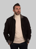 Man wearing a black jacket over a beige turtleneck on a white background