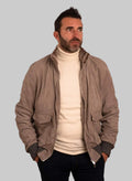 Man wearing a beige jacket over a white turtleneck on a white background